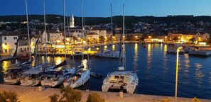 A marina at dusk with multiple boats docked, a church in the background, and a town across the water. - Salsa Brac (Supetar)