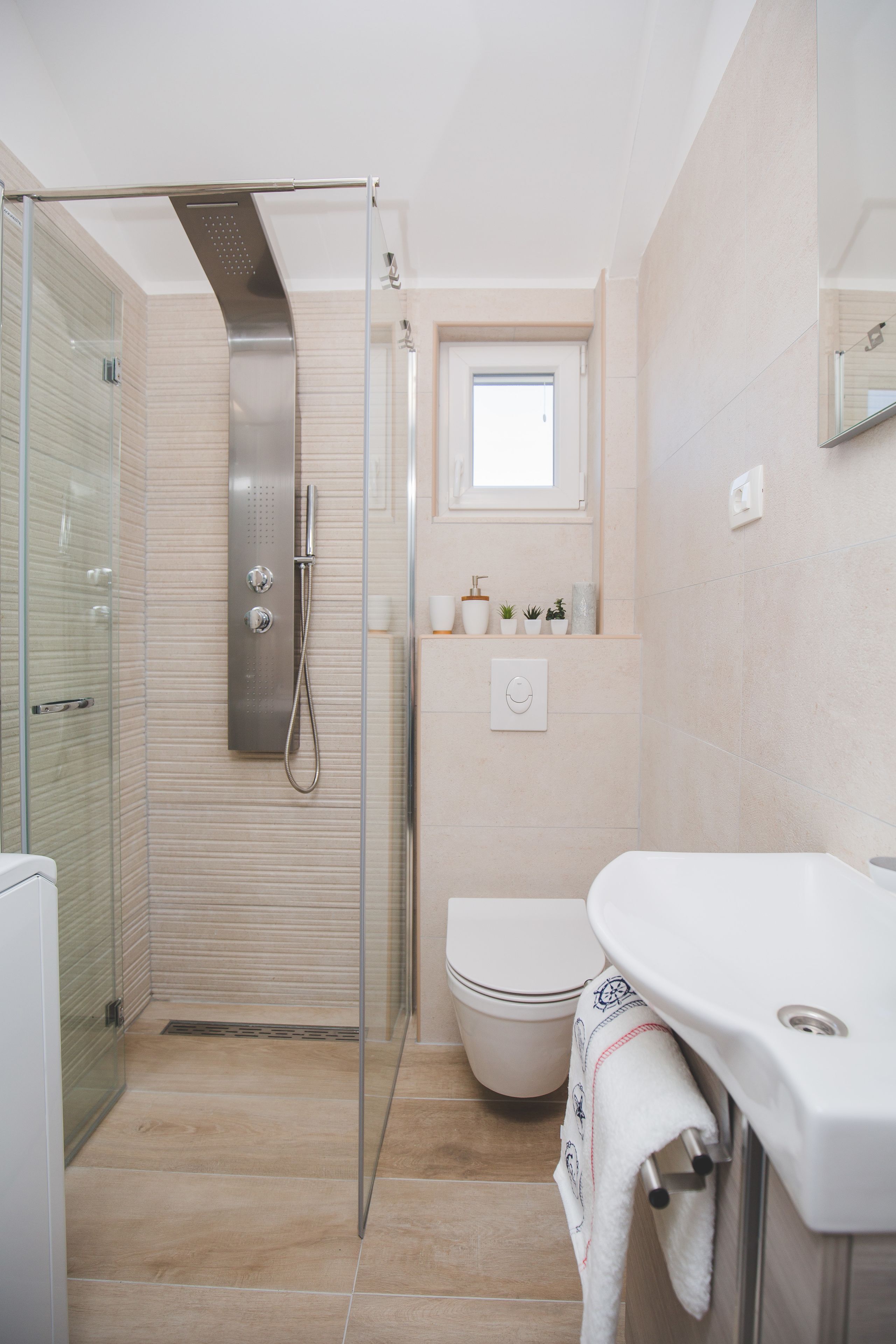 A modern bathroom with a glass-enclosed shower, a white toilet, and a sink with a towel hanging on the side.