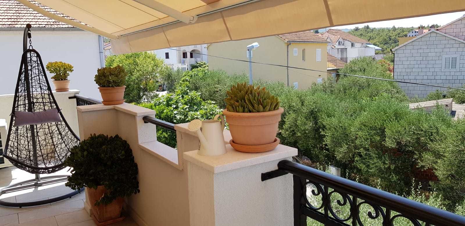 Un balcon agrémenté d’un fauteuil suspendu, de plantes en pot et offrant une vue sur les maisons voisines.