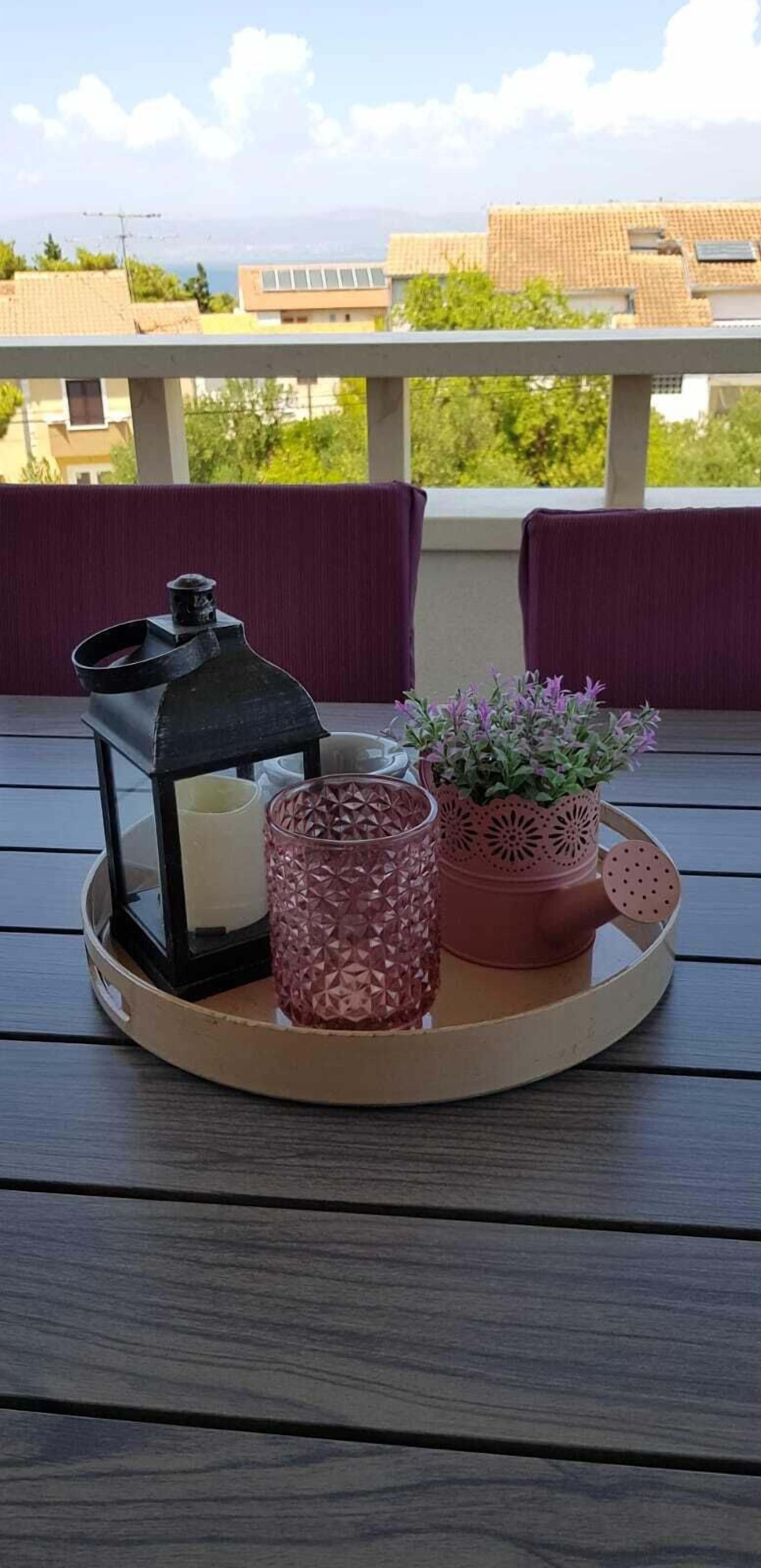 A tray with a lantern, candle, and potted plant on a wooden deck with a view of buildings and trees.