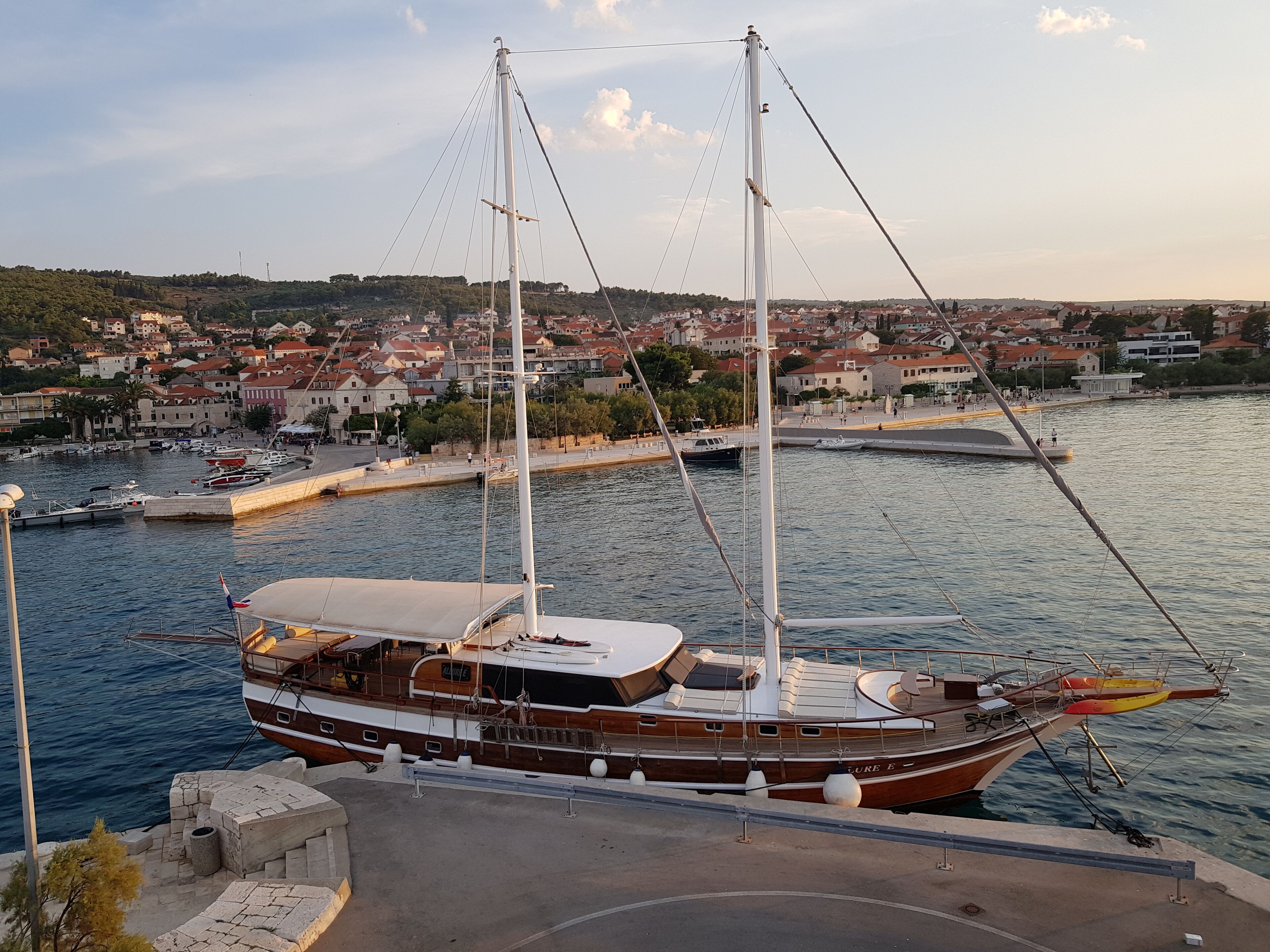 A large wooden sailing boat docked at a marina with a town in the background.