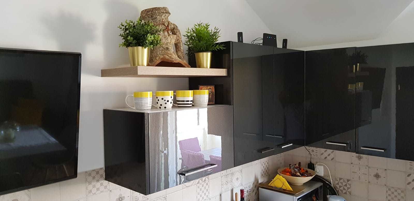 A modern kitchen with black cabinets, a built-in refrigerator, and a wooden shelf with plants and decorative items.