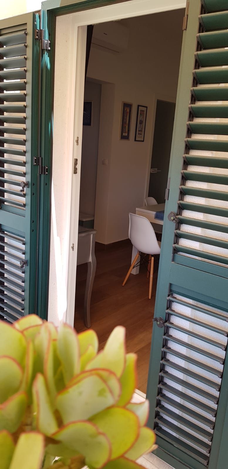 A room with a white chair, a small table, and a door with green shutters.