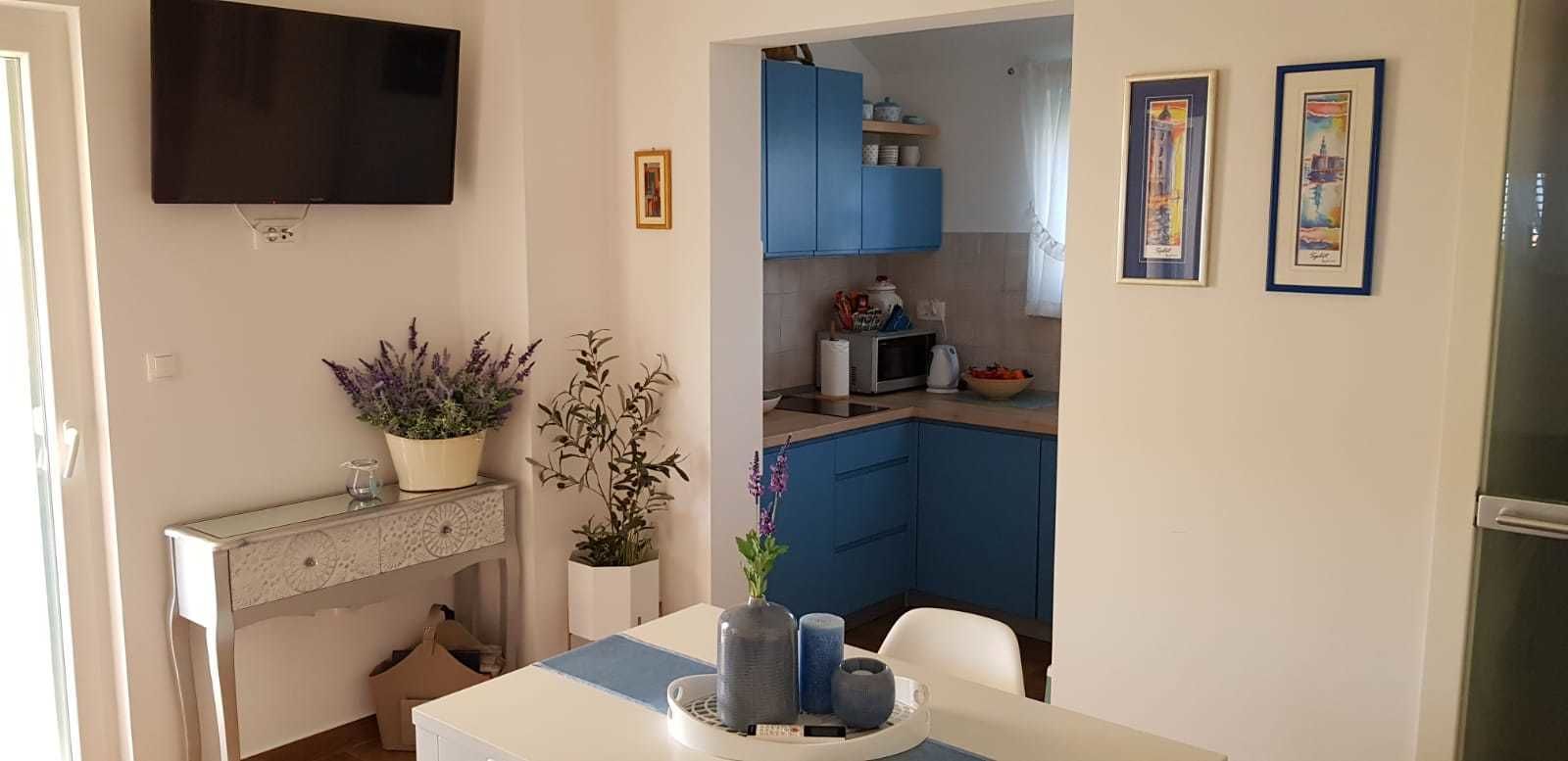 Una cucina moderna con mobili blu, una televisione a schermo piatto e due quadri appesi al muro.