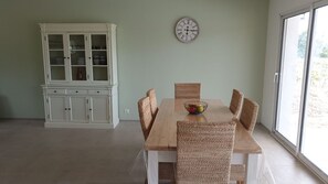 Un comedor con una mesa de madera y sillas tejidas, un armario blanco y un reloj de pared.