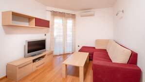 A modern living room with a flat-screen TV, wooden furniture, a red sofa, and a window with curtains. - Villa Tucepi Apartment 2 (4+1) (Tucepi)