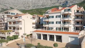 A multi-story residential building with balconies, a parking garage, and a mountainous backdrop. - Villa Tucepi Apartment 2 (4+1) (Tucepi)