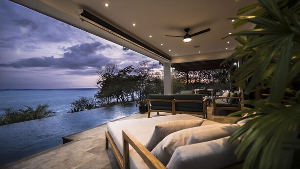 A modern outdoor seating area with a view of the sea, a ceiling fan, and a dining area with a table and chairs. - Your Dream Costa Rica Villa - Ocean View Lap Pool - Private Chef-Secret Beach (Puerto Carrillo)