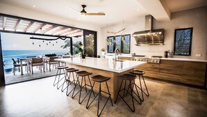 A modern kitchen with a large island, bar stools, and a view of the ocean. - Your Dream Costa Rica Villa - Ocean View Lap Pool - Private Chef-Secret Beach (Puerto Carrillo)