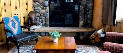 Una habitación acogedora con chimenea de piedra, un banco de madera, un tapete estampado y una mesa de madera con una planta.