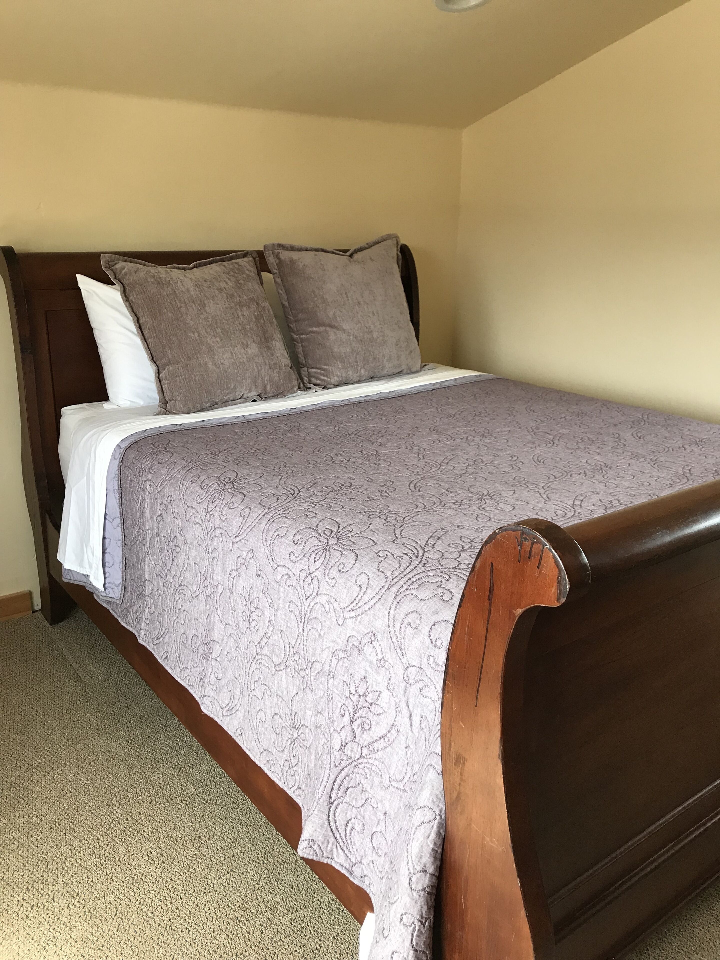 Una cama individual con cabecera y piecera de madera, colchón blanco y colcha estampada.