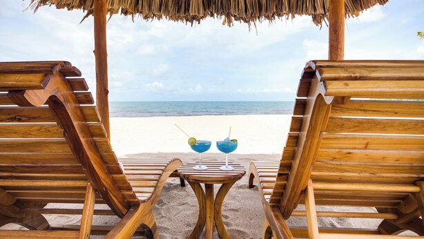 A wooden beach chair and umbrella setup with a table and two drinks in the sand, overlooking the ocean. - Luxury Beachfront Studio with swim up pool bar (Placencia)