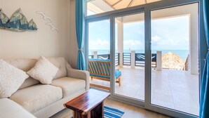 A room with a sofa, a wooden coffee table, and a view of the sea through large sliding doors. - Luxury Beachfront Studio with swim up pool bar (Placencia)