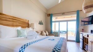 A hotel room with a large bed, a television, a kitchenette, and a view of the beach. - Luxury Beachfront Studio with swim up pool bar (Placencia)