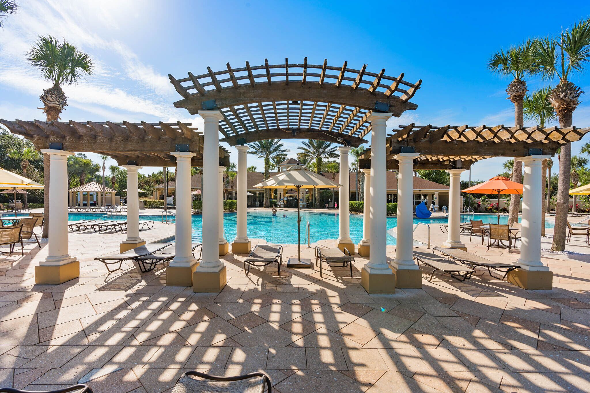 A pool area with a pergola, sun loungers, and palm trees.