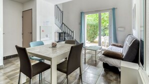 A modern living room with a dining area, a staircase, and a sliding glass door leading to a garden.