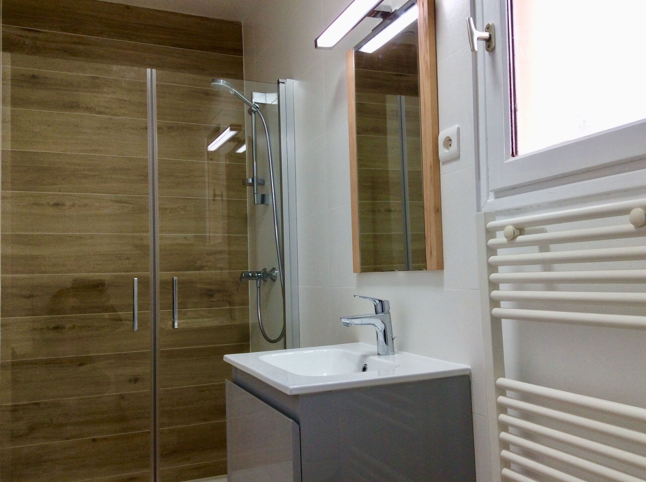 Une salle de bain moderne avec une douche à l’italienne en verre, un lavabo blanc et un miroir au-dessus.