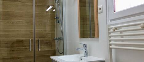Une salle de bain moderne avec une douche à l’italienne en verre, un lavabo blanc et un miroir au-dessus.