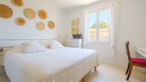 Un dormitorio con una cama grande, una silla de madera, un escritorio y una ventana con cortinas.