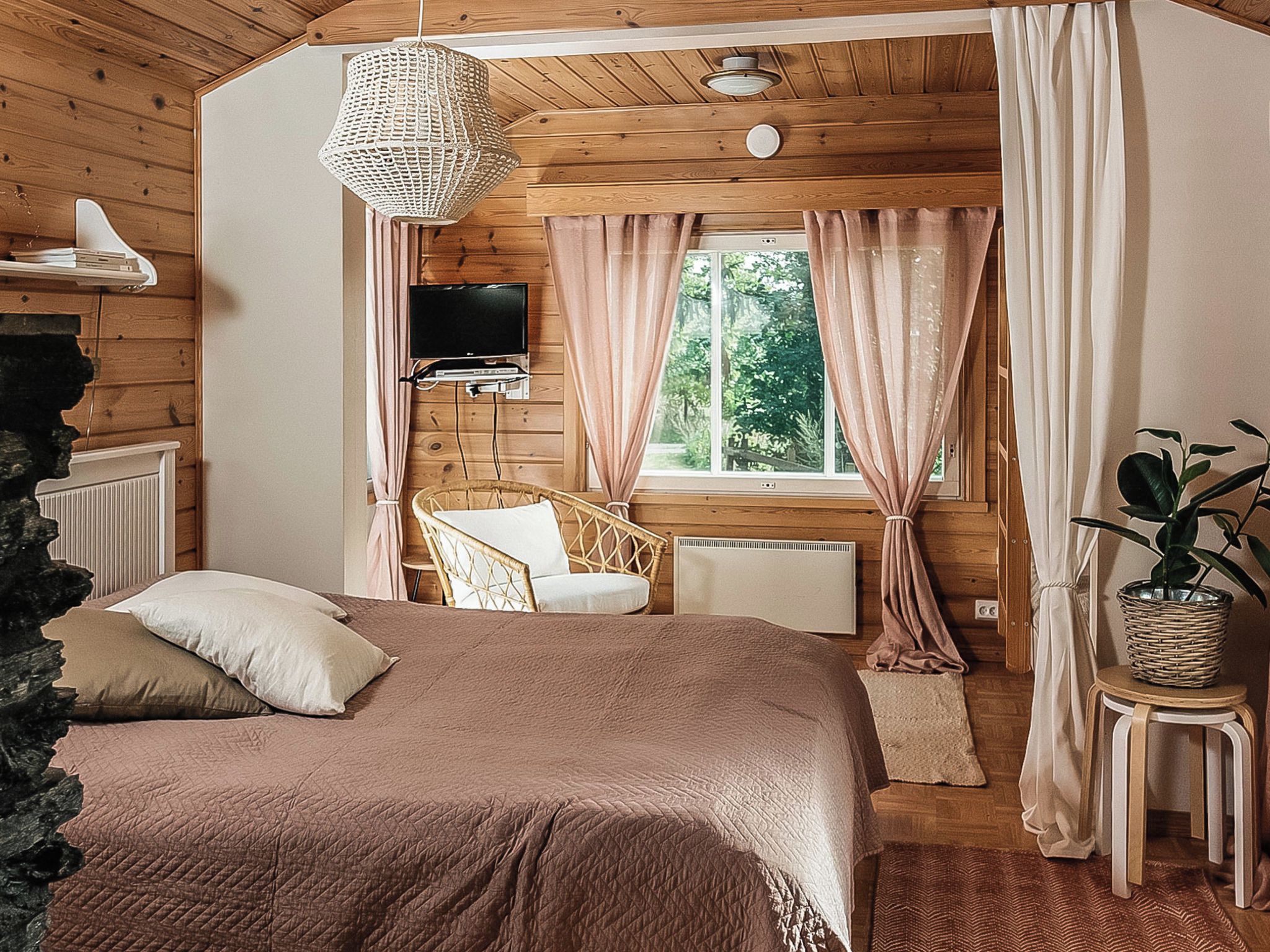 Een gezellige slaapkamer met een bed, een stoel, een televisie en een raam met gordijnen.