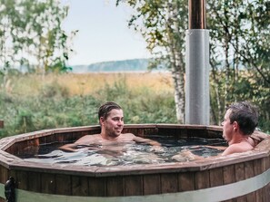A hot tub with two people inside, surrounded by a natural landscape.