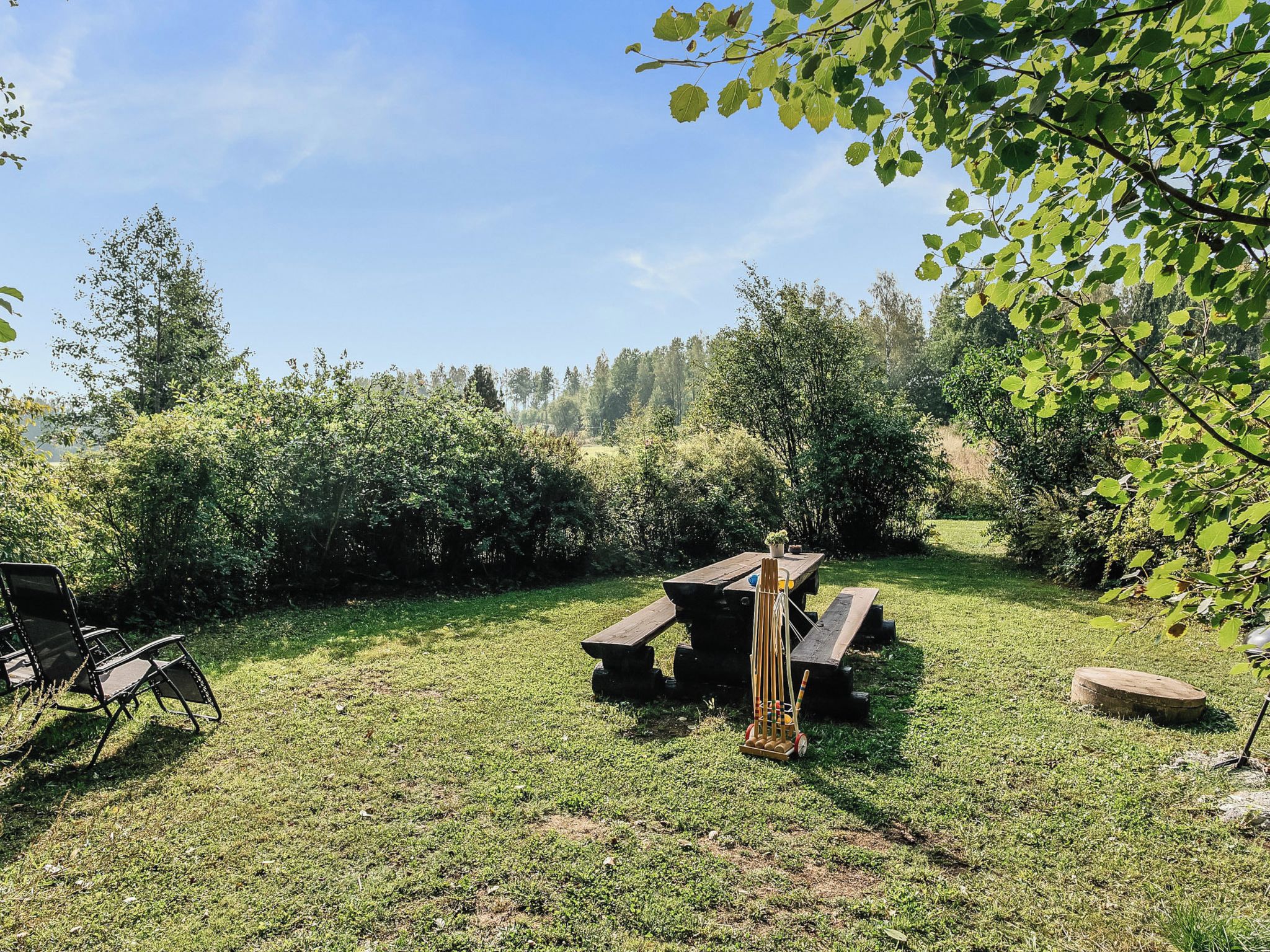 Zona de picnic con mesa y sillas, rodeada de césped y árboles.