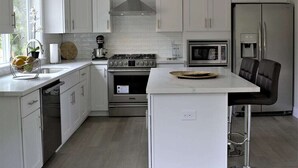 A modern kitchen with white cabinetry, a central island, a stove, oven, microwave, and refrigerator. - Modern, new and close to lake (Lake Oswego)