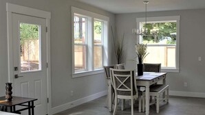 A dining area with a white table and chairs, a vase with flowers, and large windows with a view of the outside. - Modern, new and close to lake (Lake Oswego)