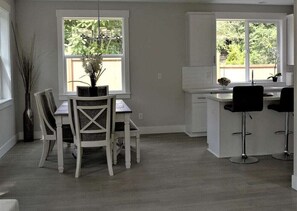 Een moderne keuken met witte kasten, een eethoek met een witte tafel en stoelen, en twee barkrukken.