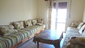 A room with two sofas, a wooden table, and a door with a view. - Residence Chems Corniche Martil 3915 (Martil)