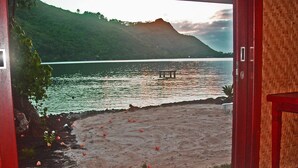 Une vue depuis une pièce dont la porte en bois donne sur une plage, avec une montagne en arrière-plan.