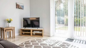 Una sala de estar con un sofá de cuero marrón, un mueble bajo para televisión de madera y una pequeña mesa con un jarrón de flores amarillas.