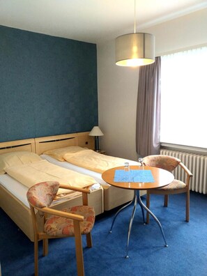 A hotel room with a bed, a round table, two chairs, a lamp, and a window with curtains. - Der Quellenhof (Helmstedt)