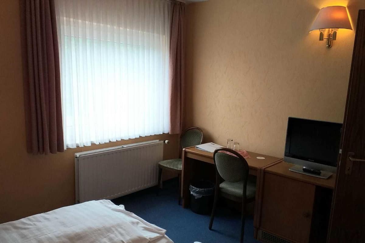 Ein Hotelzimmer mit Bett, Schreibtisch, Stuhl, Fernseher und einem fenster mit Vorhängen.