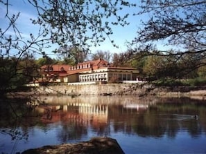 A lakeside hotel with a red roof and a reflection in the water. - Der Quellenhof (Helmstedt)