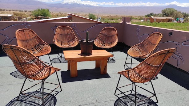 Un patio en la azotea con sillas de mimbre y una mesa de madera, con vistas a un paisaje montañoso.
