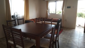 Un comedor con mesa y sillas de madera, un ventilador y un sofá con cojines.