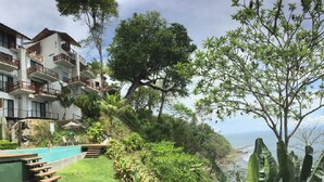 Un hotel de varios pisos con balcones, piscina y abundante vegetación.