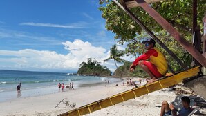 Escena de playa con gente, un socorrista y una torre de salvavidas.