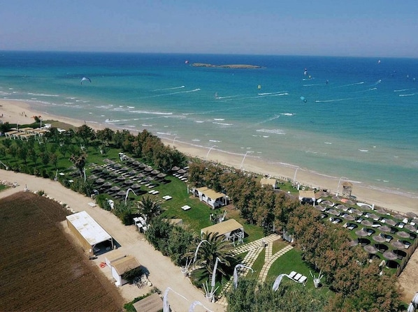 Vista aérea de un complejo turístico en la playa con varias cabañas tipo bungalow, una playa de arena y una vista despejada del mar.