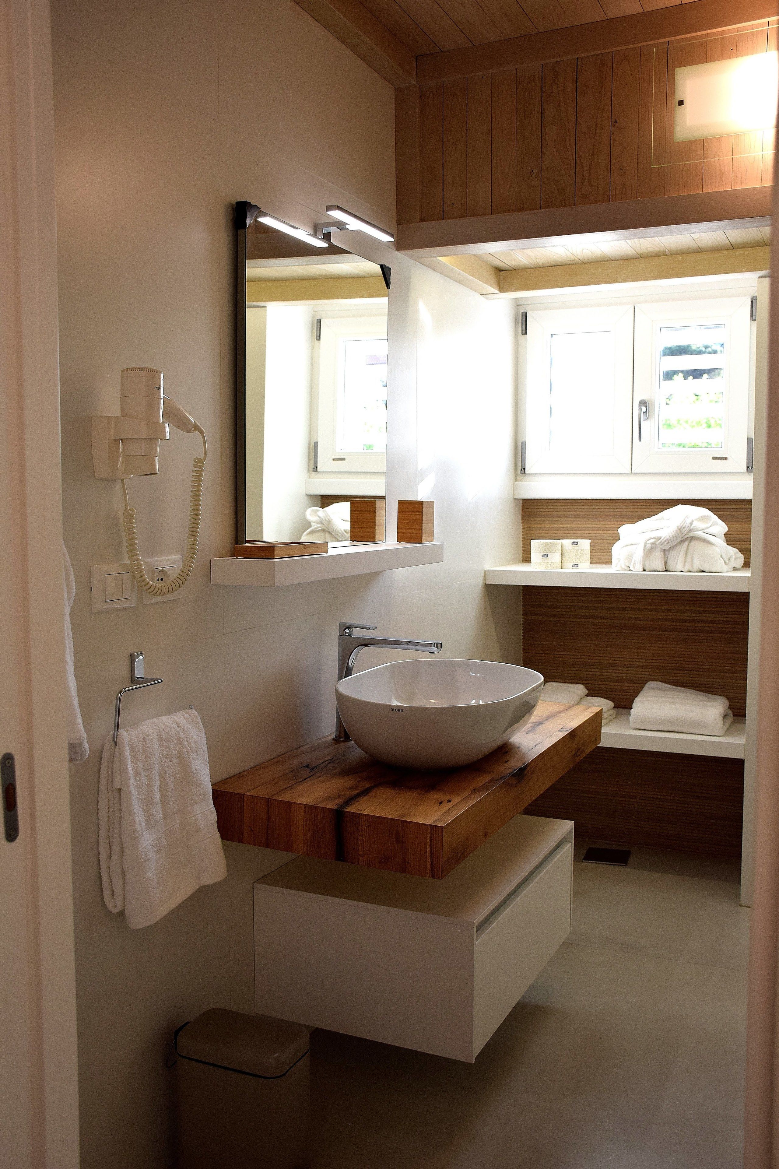 Een moderne badkamer met een houten wastafelmeubel, een grote spiegel, een witte wasbak en een handdoekrek.