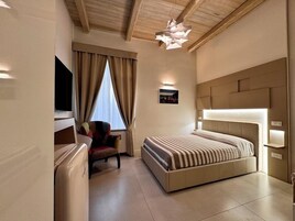 A modern hotel room with a large bed, a desk, a chair, and a television.