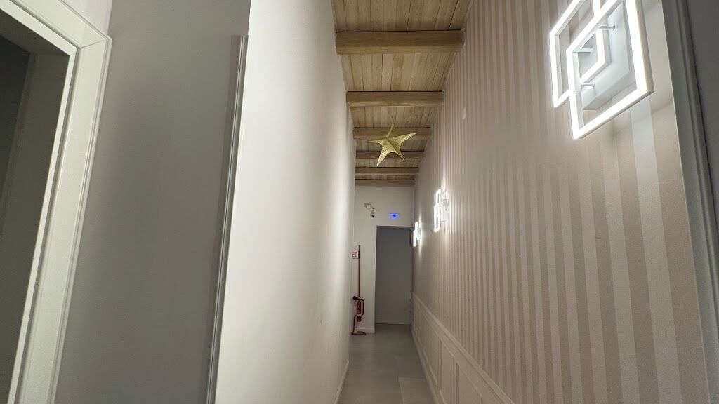 Ein schmaler Korridor mit Holzboden, einer sternförmigen Leuchte und einer gestreiften Wand.