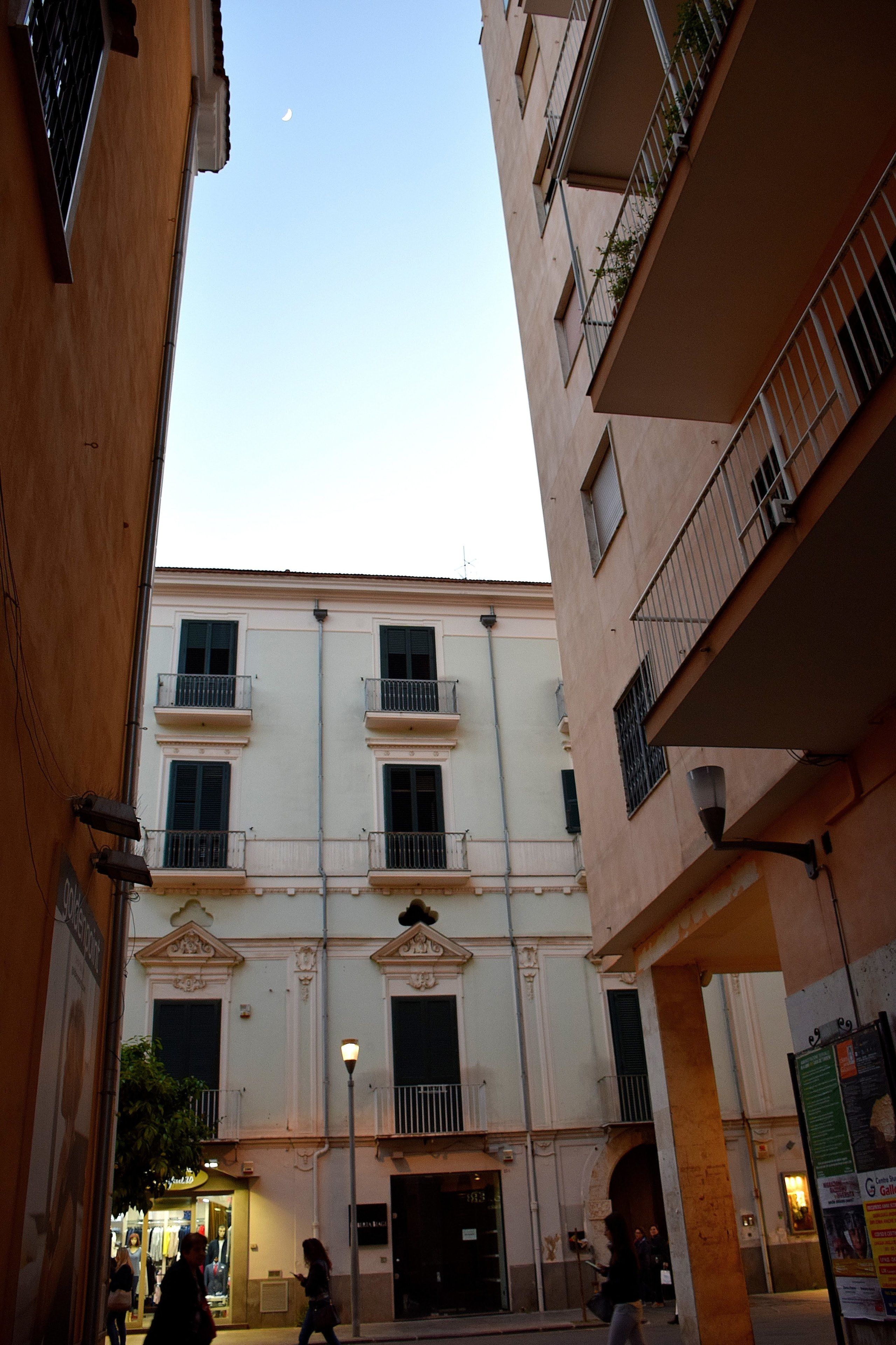 Une rue étroite bordée d’un immeuble doté de balcons et abritant un commerce au rez-de-chaussée.