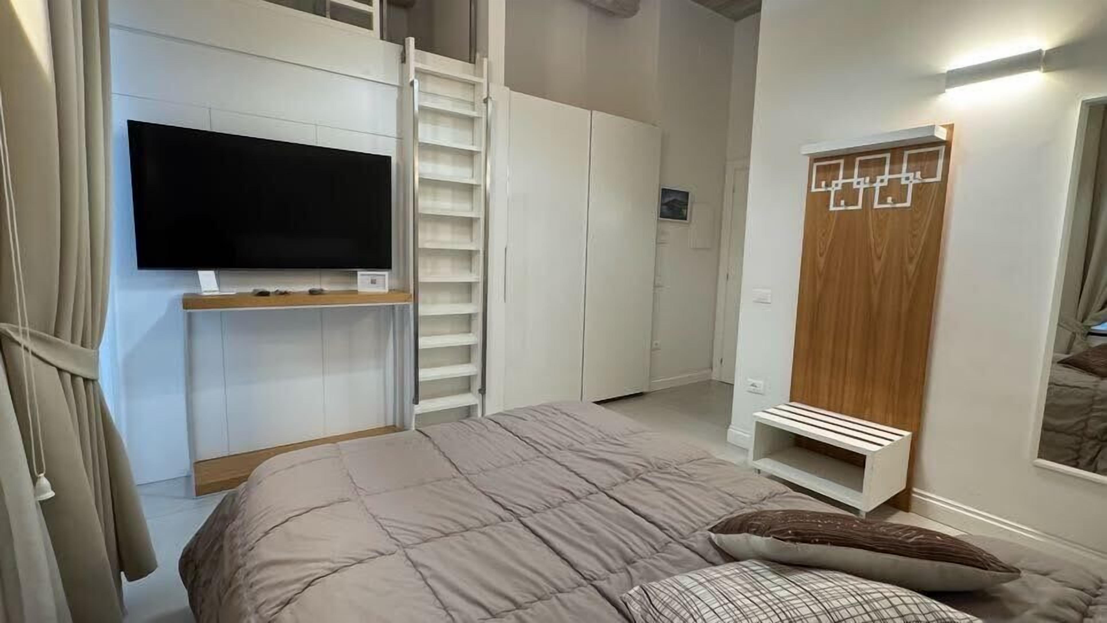 A bedroom with a bed, a TV mounted on the wall, a wardrobe, and a closet.