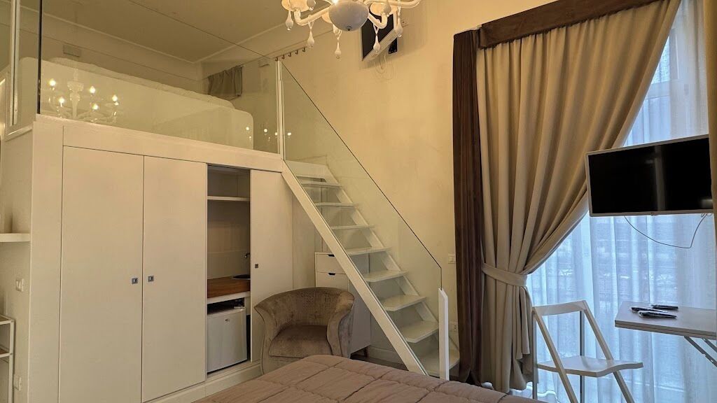 A bedroom with a bed, a wardrobe, a desk, a chair, a TV, and a staircase.