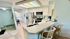 Una cocina moderna con una isla central, electrodomésticos de acero inoxidable y taburetes de bar blancos.