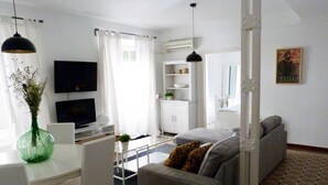 A modern living room with a grey sofa, a dining table with chairs, a TV, and a white cabinet. - Very luminous apartment in the corner of the Cathedral, in the Arenal district (Sevilla)