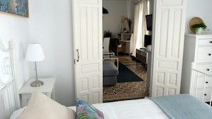 A bedroom with a bed, a bedside table with a lamp, a dresser, and a door leading to a bathroom. - Very luminous apartment in the corner of the Cathedral, in the Arenal district (Sevilla)
