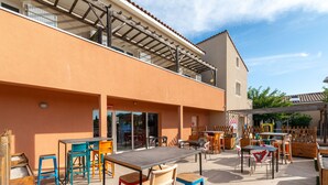 Un patio al aire libre con mesas y sillas, una zona de estar cubierta y un edificio con techo de tejas.